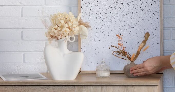 Woman putting beautiful dry flowers in vase onto wooden dresser indoors, closeup
