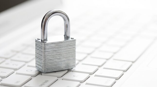 A metal padlock sitting on a white laptop keyboard representing digital security with computer keyboard data sits top