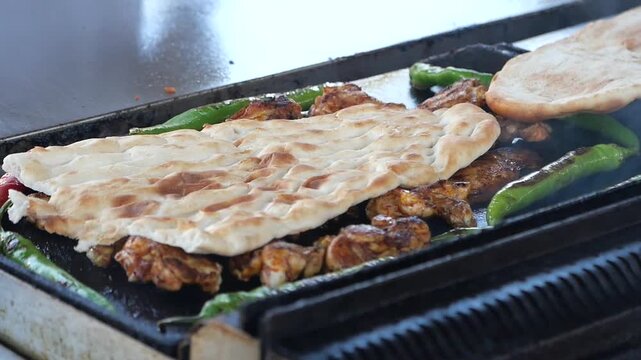 Chef grilling traditional chicken thighs on flat top stove with green peppers and pita bread