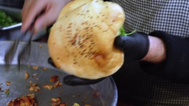 Street food chef filling pita bread with chicken kebab meat and fresh vegetables