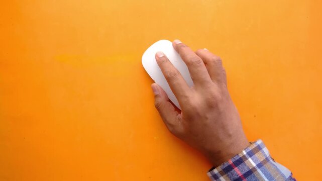 Close up of person hand using white wireless computer mouse on orange background