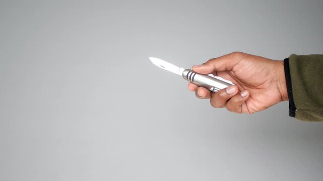 A close up of a hand holding and rotating a multi tool knife on a plain background, creating a dynamic and focused visual clip
