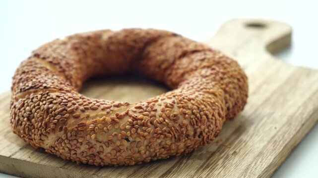 Freshly baked turkish simit, a traditional sesame seed bagel, rests on a rustic wooden cutting board, captured in a dynamic close-up shot on white background
