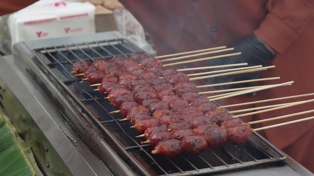Red meatball skewers cooking on a street food grill