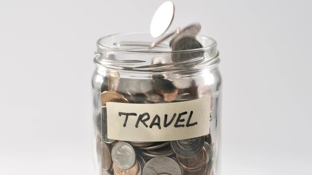 Close-up shot of coins falling in slow motion into a coin jar labeled 'Travel'.