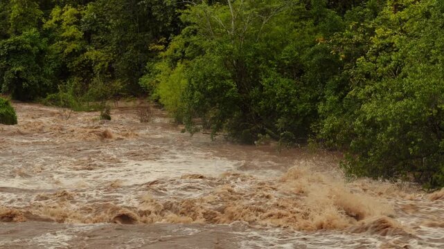 Rushing turbulent muddy waterfall and forest river rapid after overnight heavy rainstorm
