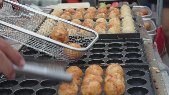 Street food vendor cooking golden round snacks in a griddle pan