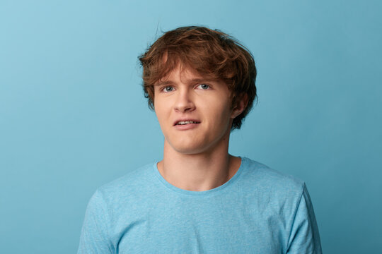 Young man with a hesitant uncertain expression looking aside. Hesitant man with a tight-lipped uneasy look against a blue studio background.