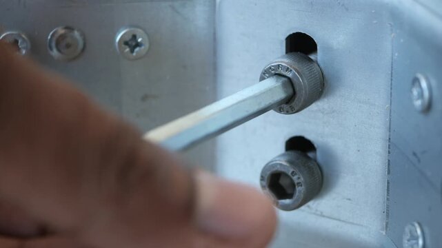 Close up of person using allen key to tighten hex bolt on metal structure in construction site