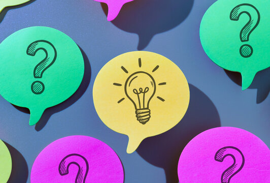 Yellow speech bubble with drawn lightbulb surrounded by green and pink question mark on a blue background. Idea generation, solution, breakthrough, innovation concept.