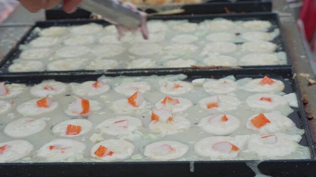 Hand preparing white round snacks in a street food griddle