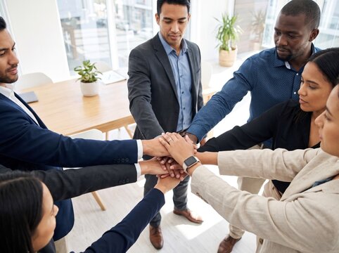 Multiracial group of professional business colleagues stacking hands in a circle for a team huddle in a bright modern office, representing unity, collaboration, partnership, and corporate success.