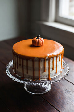 Round layered cake with caramel drip glaze and pumpkin on glass cake stand