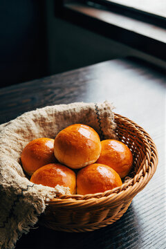 Five glossy golden baked buns in wicker basket lined with coarse linen
