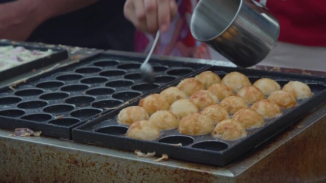 Vendor arranging golden round snacks on a street food griddle