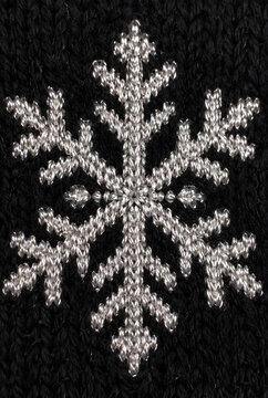 Close up of a silver embroidered snowflake on black knitted fabric winter decoration