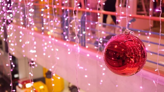 Red shiny christmas ornament hanging amidst a cascade of sparkling pink fairy lights, creating a festive and reflective holiday ambiance in motion