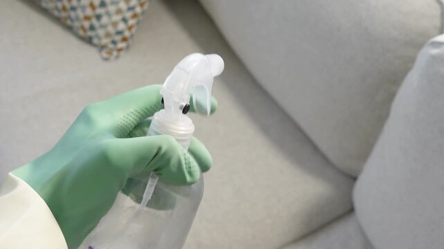 Hand in glove spraying disinfectant on couch for cleaning and sanitizing motions