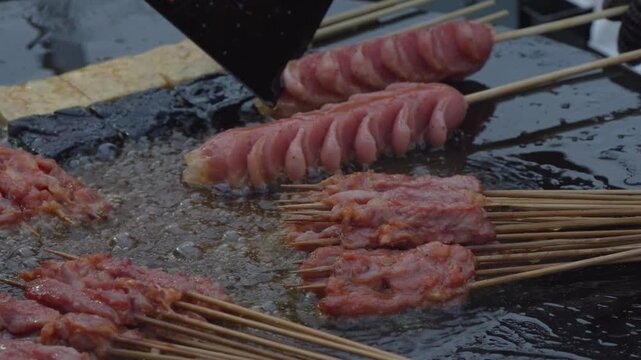 Vendor arranging sausage skewers on a street food barbecue grill