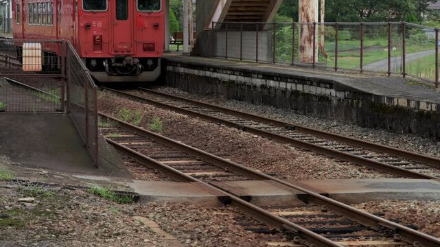 ローカル線の駅に到着する赤い気動車の鉄道風景