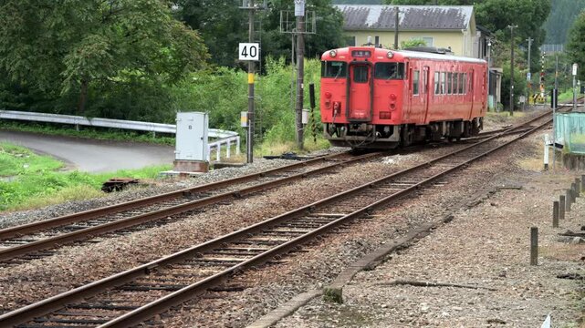 ローカル線の駅に到着する赤い気動車の鉄道風景