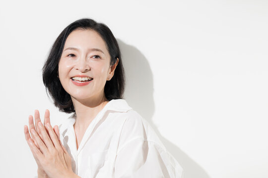 [白背景]喜びながら感謝する50代の日本人女性、成功や達成、合格、採用、嬉しい気持ちを表現する笑顔の人物