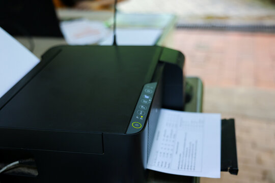 Black office printer with paper document on desk creating functional workspace scene, emphasizing everyday printing technology and office productivity