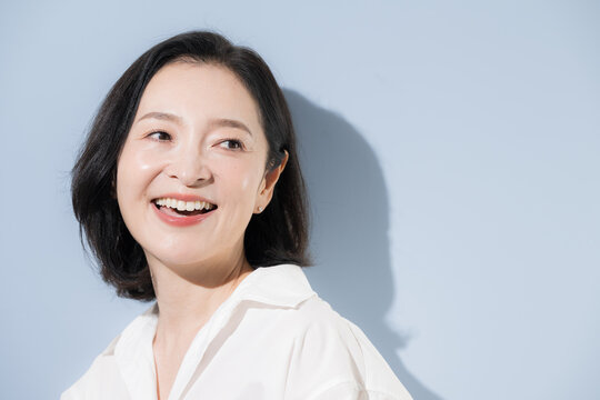 [水色背景]笑顔で明るい表情を見せる50代の日本人女性、美容や健康、自然体、前向きなミドル女性のポートレート振り返る