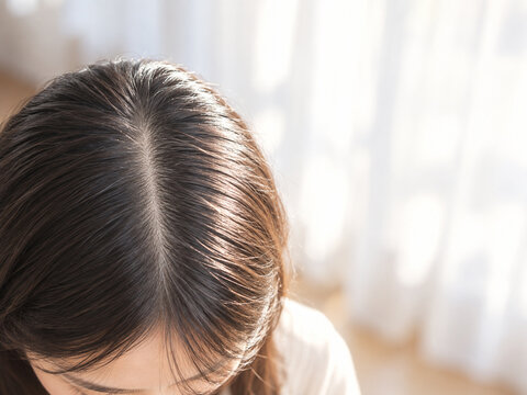 朝の光が分け目に差し込む30代女性の頭皮の接写