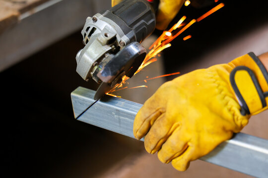 Metalworker cutting aluminum bar with angle grinder, creating bright sparks during workshop fabrication and wearing protective gloves