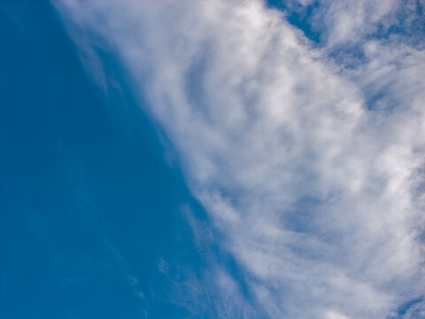 A long diagonal bank of wispy white clouds crosses the right side of the frame beside a broad area of deeper blue sky. The open sky offers a calm backdrop with soft blue tones and an airy composition.