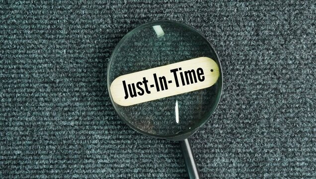 A magnifying glass with the words Just-in-time. production and inventory strategy where materials and products are received or manufactured only as they are needed.