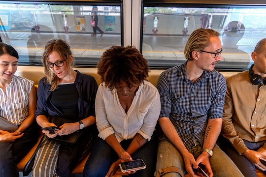 Diverse group of people sitting on a train, using their phones.