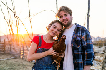 A couple holding a chicken on a farm at sunset, smiling warmly. © Rawpixel.com
