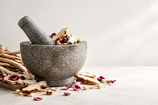 Stone mortar and pestle with dried mandrake roots and petals, herbal apothecary still life