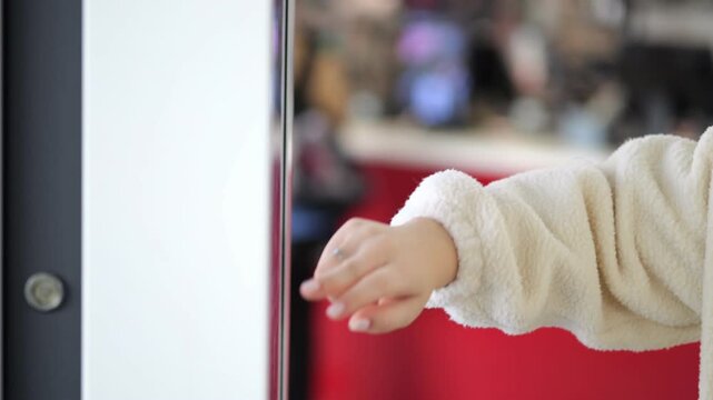 Hand touches interactive screen door. Background shows blurred indoor space. Red wall visible behind person. Person wears white fleece jacket. Door has metal handle and hinges