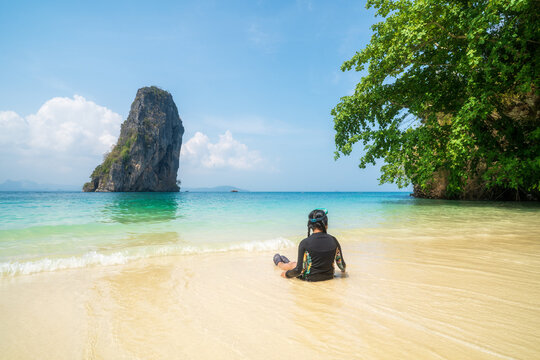 summer asian child sitting relax on white sand beach or kid girl wear swimsuit and diving goggles in blue sea with tourist boats at ko poda island in krabi thailand for people holiday vacation travel