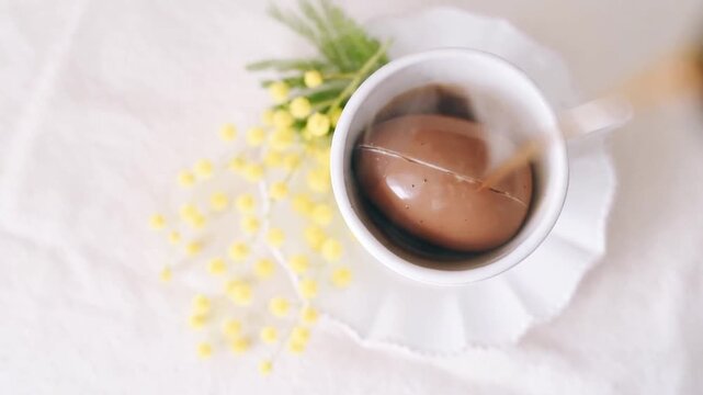 Pouring hot coffee over chocolate egg in white cup on decorated table in slow motion.