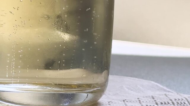 Sparkling white wine or soda with carbonated bubbles rising in glass cup closeup motion footage.