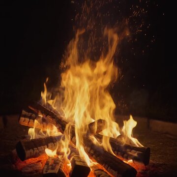 Bright orange campfire burning with glowing embers and sparks in the dark night.