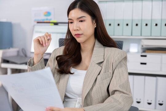 Professional woman reviewing document in modern office with focused expression and organized workspace, business planning and administrative work concept