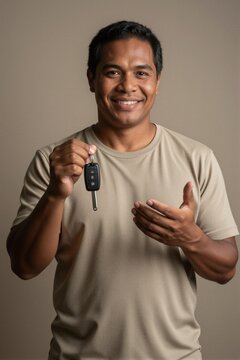 A middle-aged man with a broad smile holds up a car key fob in a studio setting, conveying happiness and satisfaction.