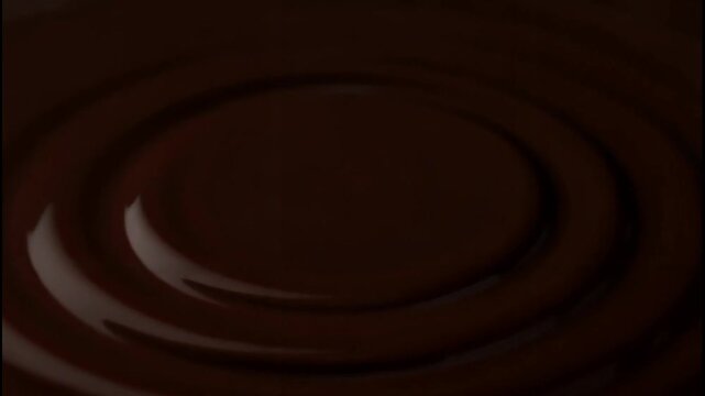 Close-up of thick chocolate pouring into a pool, creating concentric ripples and a glossy swirl pattern