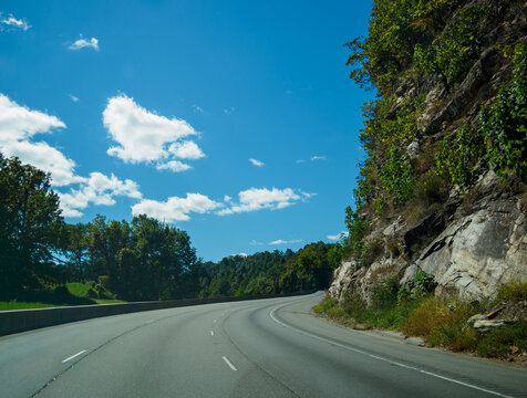 Scenic view of a winding highway cutting through a dramatic mountain pass under a blue summer sky. Ideal for travel, transportation, and road trip concepts.