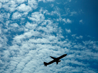Commercial airliner silhouetted against a textured blue sky filled with white altocumulus clouds. Ideal for travel, aviation, tourism, and vacation themes. © Julio