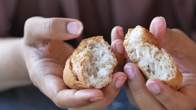 Woman's hands gently tearing fresh homemade bread in half slow motion close up, revealing soft interior texture