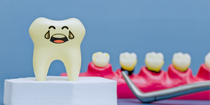 Sad crying tooth model suffering from toothache. Pediatric dentistry concept with decayed jaw model and dental tool on blue background.
