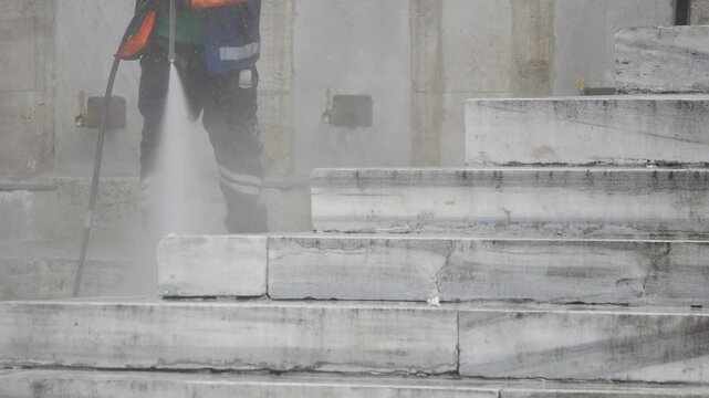 Worker pressure washing stone stairs with water spray motion