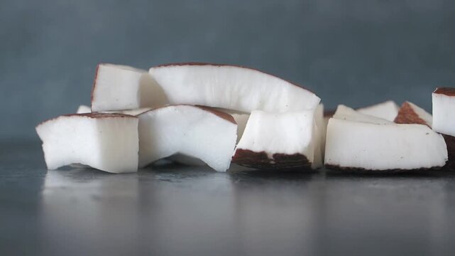 Fresh coconut chunks falling onto dark table in slow motion macro shot