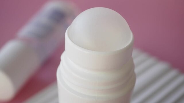 Macro shot of roll on deodorant stick with liquid on white ball over pink background